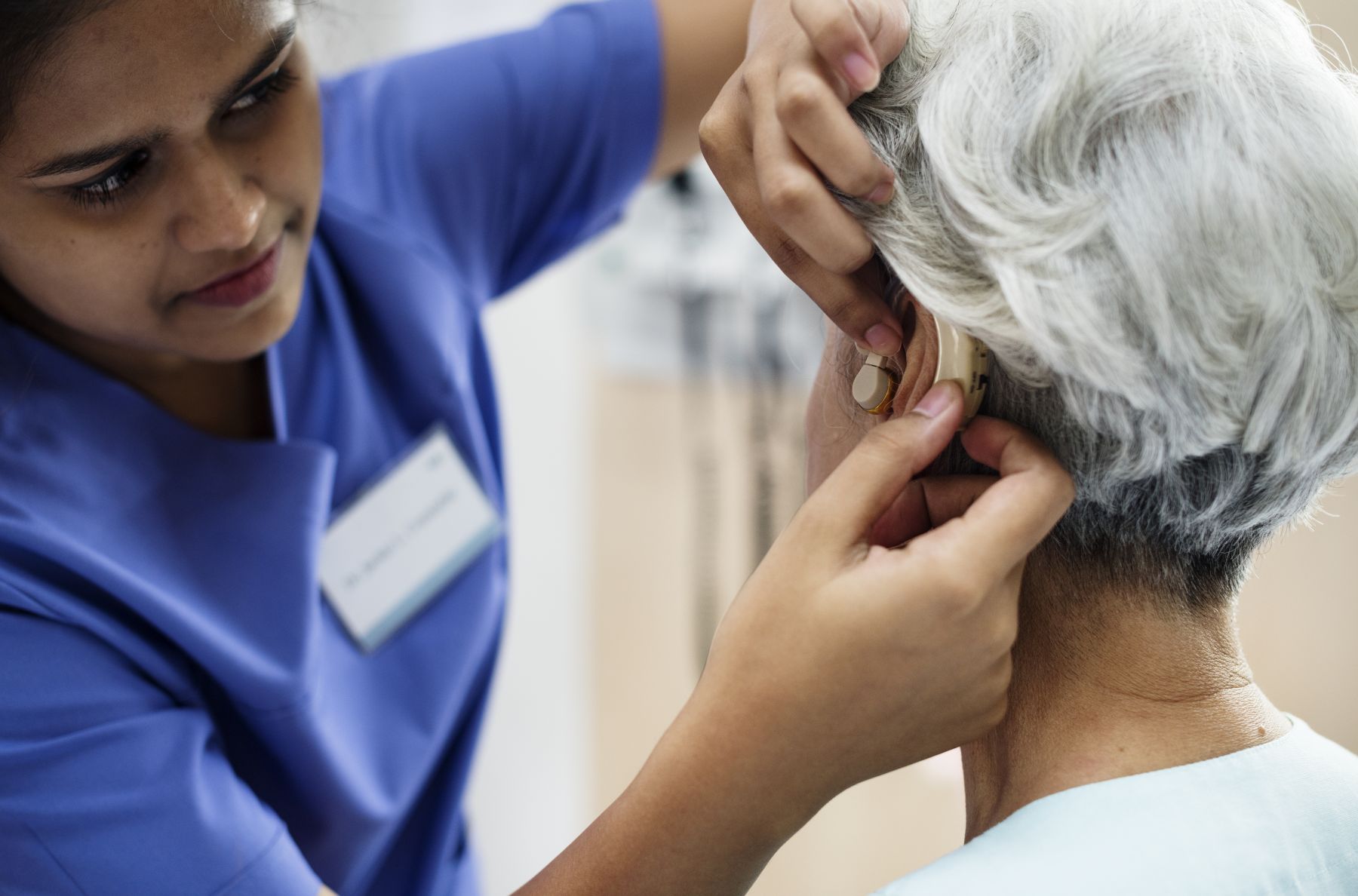 Nurse putting in Mrs. Nguyen's hearing aid.