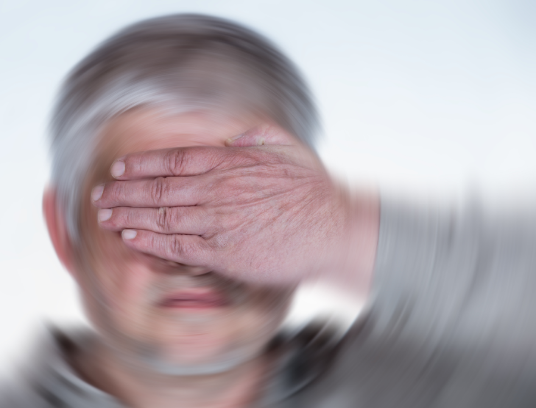 Older adult with hands over eyes, background is distorted, indicating disorientation.