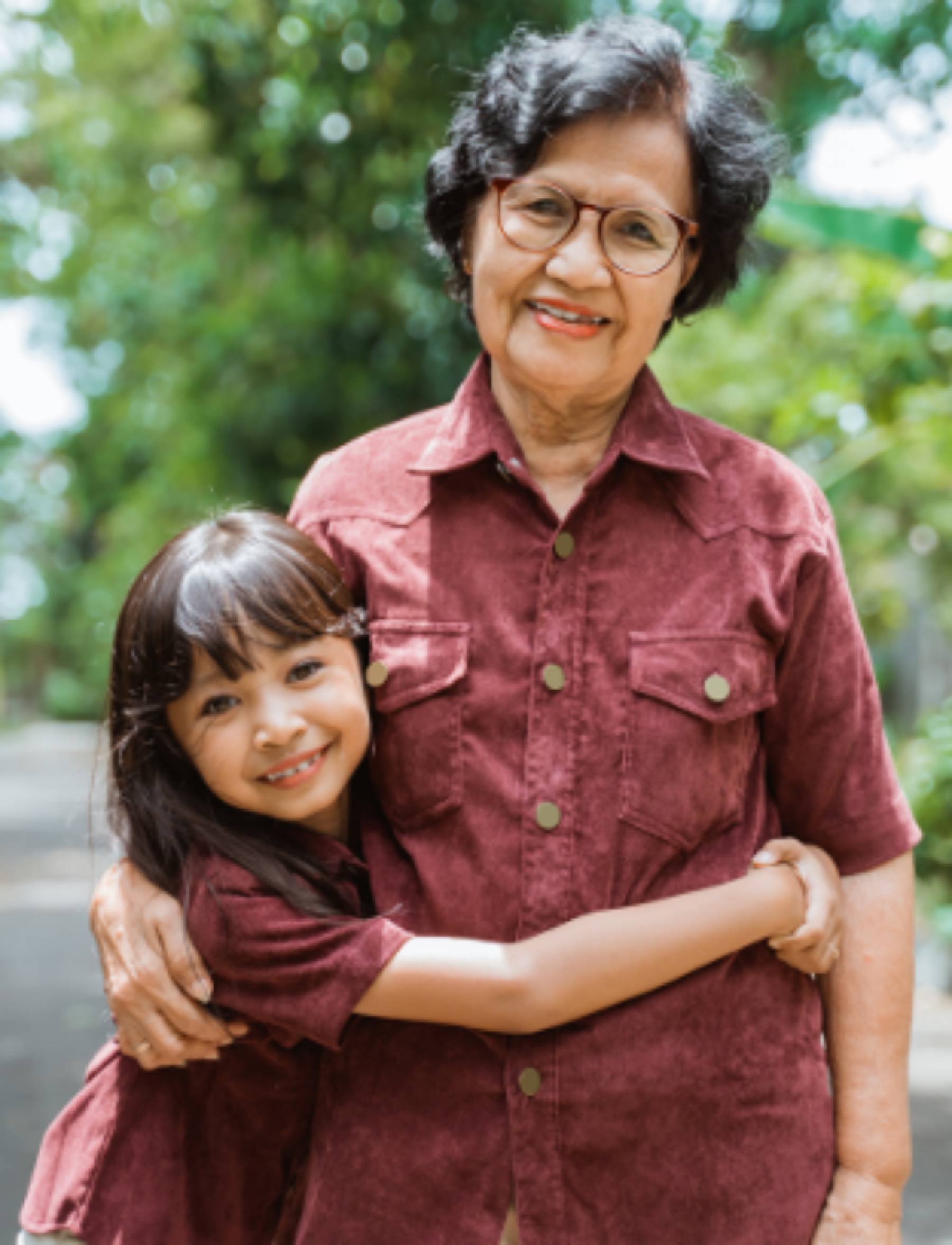 Grandmother with arm around granddaughter, outdoors.