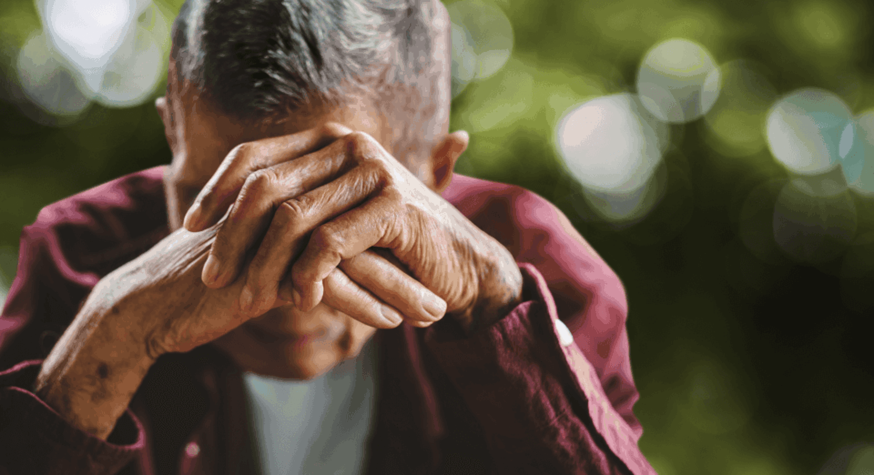 Older adult male with his head in his hands.