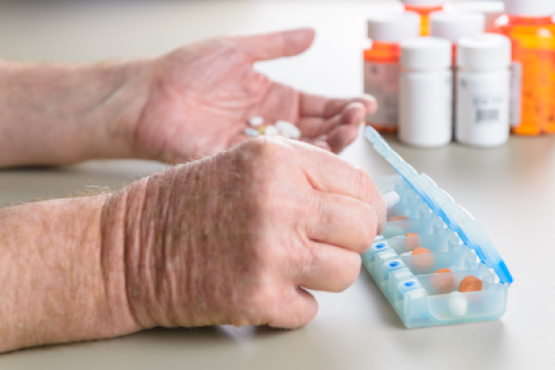 Close-up of hands sorting pills into a 7-day pill box.