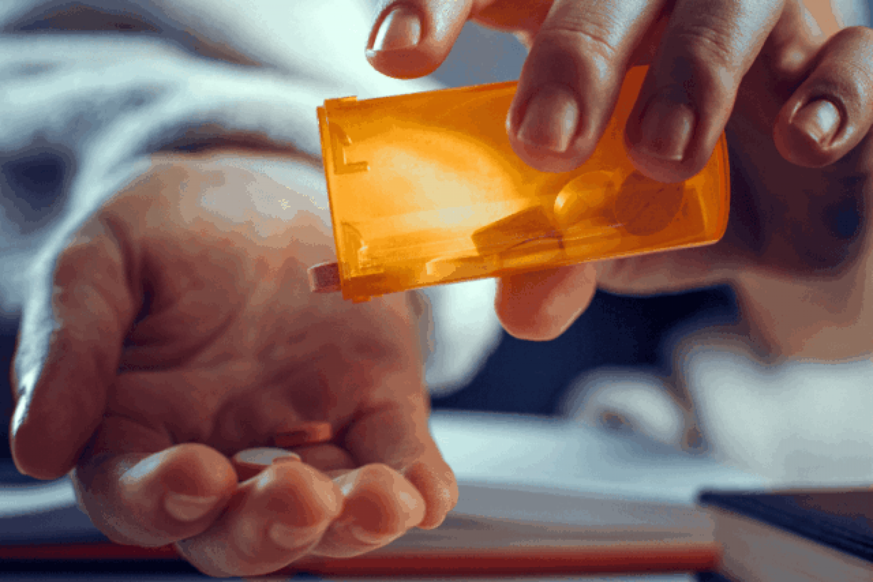 Healthcare professional shaking a pill from a bottle into their open hand.