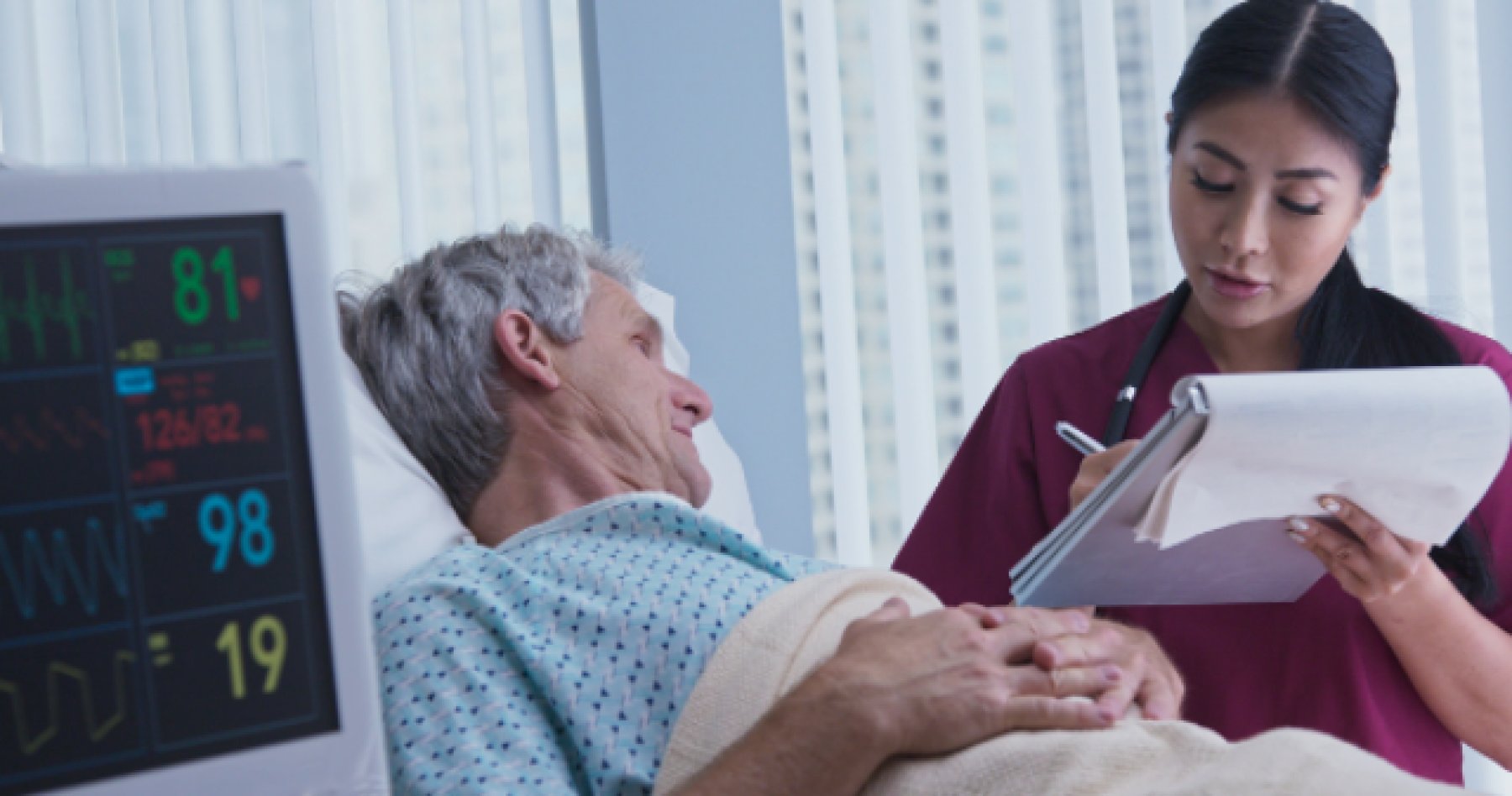 Older adult male in a hospital bed speaking with his female doctor.