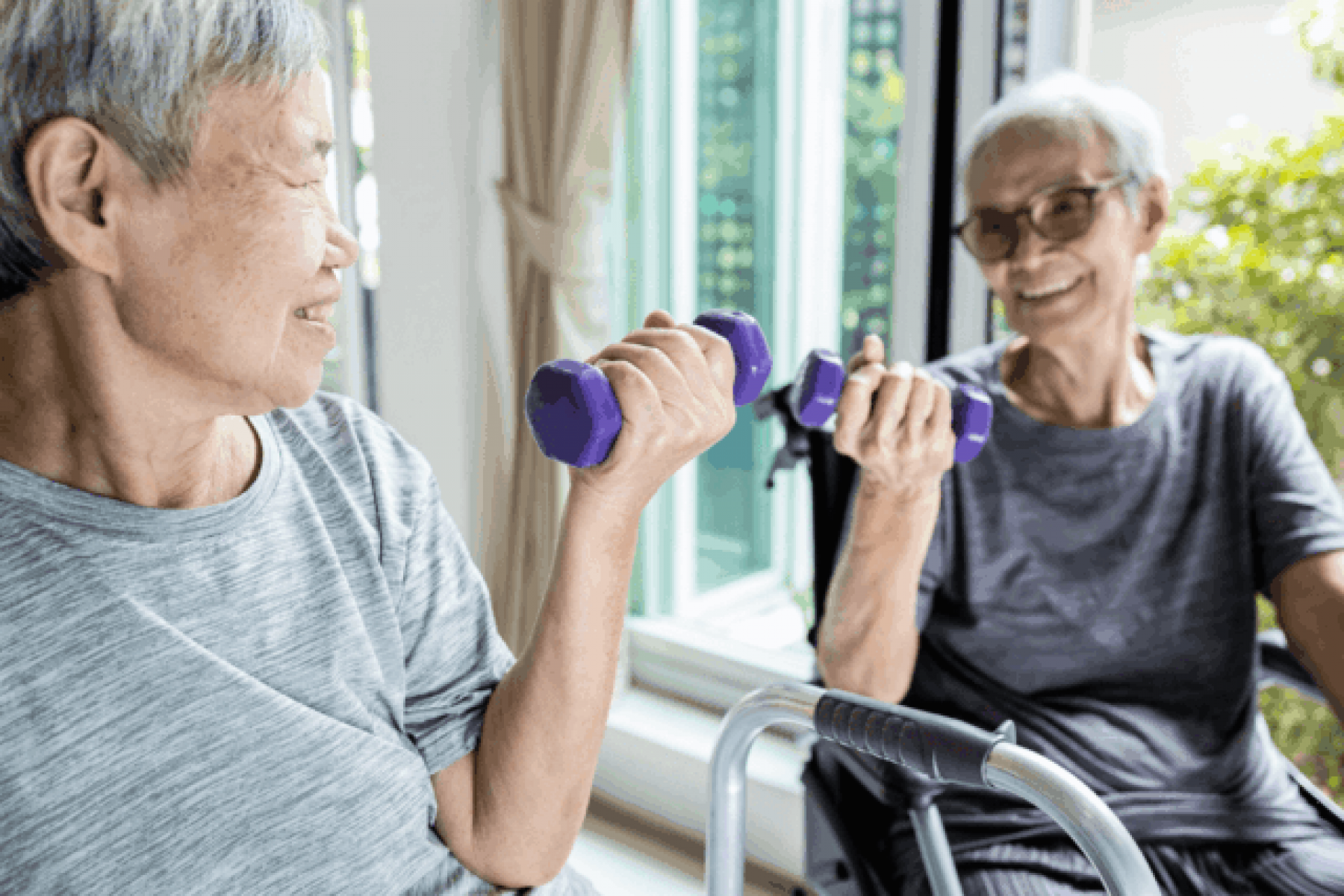 Two women lifting weights - one is sitting by her walker, the other is sitting in a wheelchair.