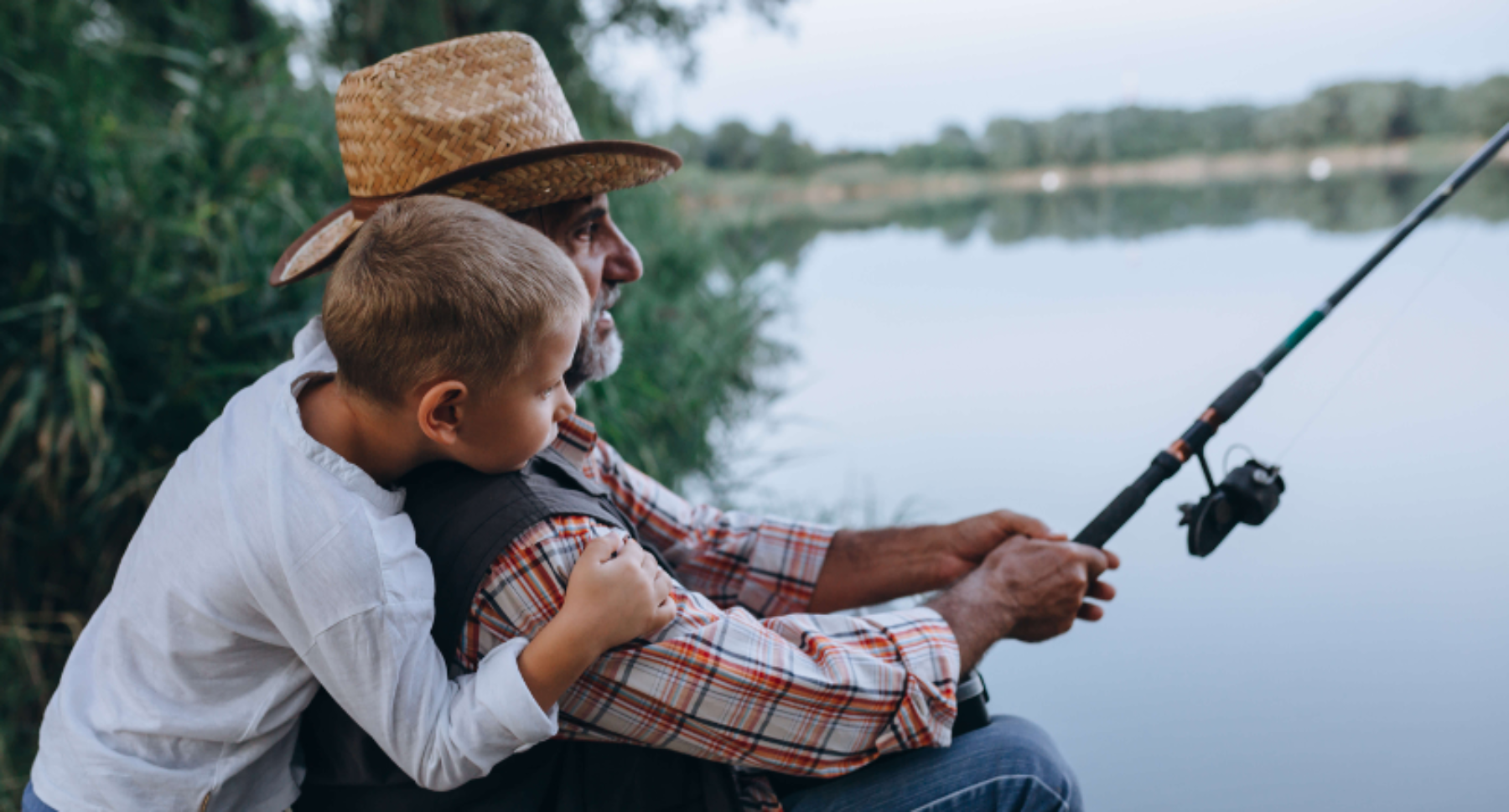 Grandfather and grandson fishing by a river.