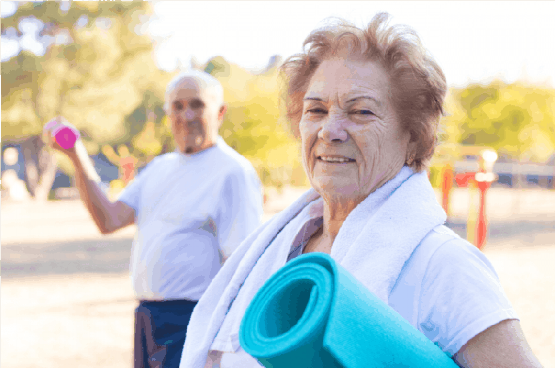 Woman in the foreground with a rolled up yoga mat under her arm, man in the background lifting a hand weight.