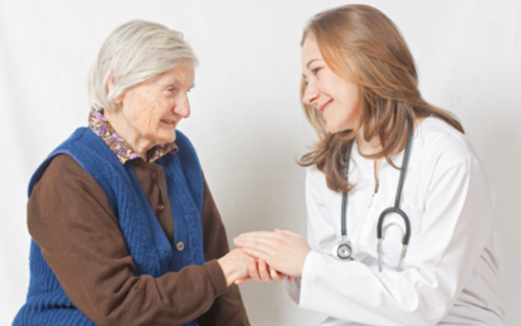 Older adult woman talking with younger female doctor, doctor looks caring and has her hands on the woman's hands.