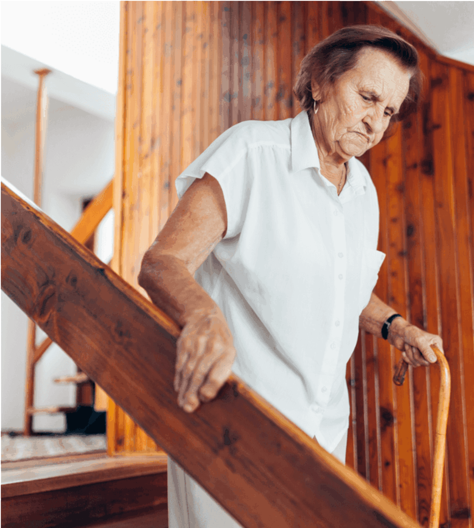 Adult woman going down a wooden staircase using a cane.