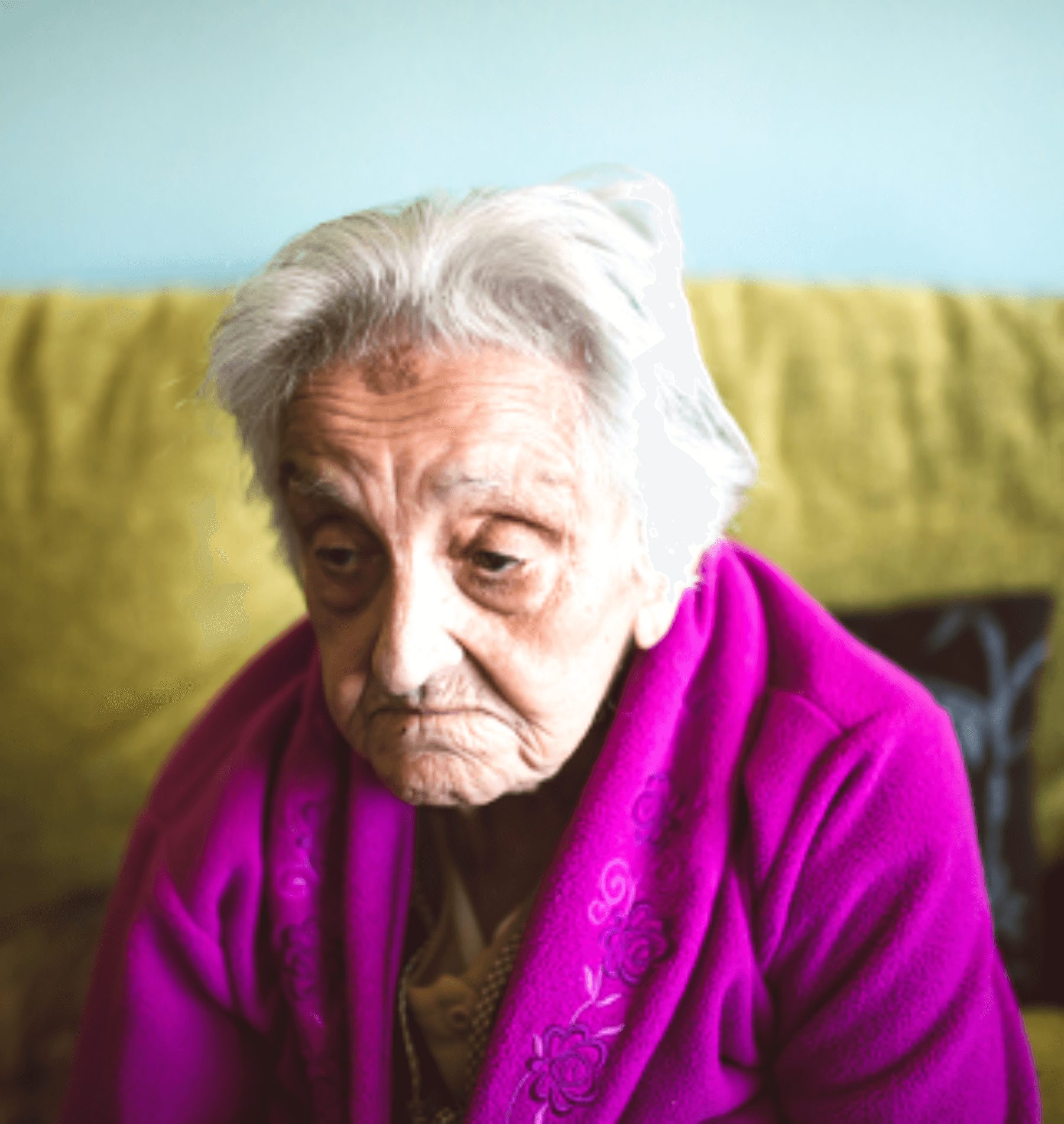 Older adult woman sitting on a sofa, looking depressed.